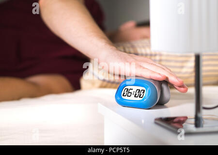 Man waking up in bed. Turning off alarm clock on nightstand or pressing snooze. Stock Photo