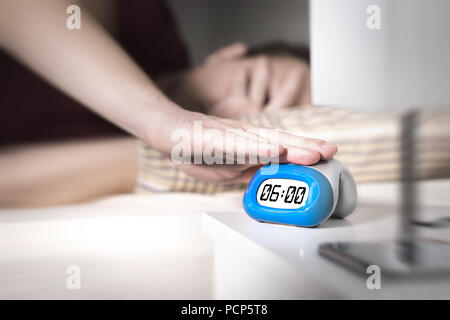 Man don't want to wake up for work in the morning. Turning off alarm clock or press snooze button with hand. Lazy person unable to get out of bed. Stock Photo