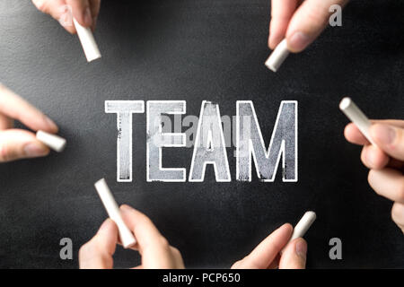 Teamwork and group work concept. Multiple people writing the word team to the same chalkboard with chalk pens. Stock Photo