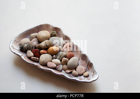 Sea stones colored in various patterns inside a glossy seashell isolated on white background Stock Photo