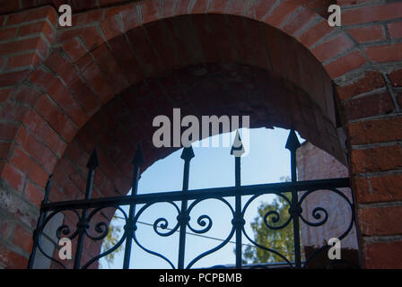 Element of ancient church architecture: an arch of red brick and openwork forged lattice. Stock Photo