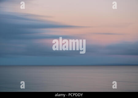 Muted blur sunrise over ocean with pink and gray clouds Stock Photo