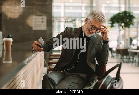 Mature business man talking on mobile phone with earphones at cafe. Smiling mature man in suit relaxing at cafe and speaking on smart phone. Stock Photo