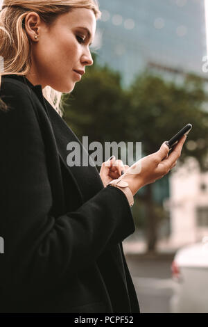 Young businesswoman requesting pickup by taxi on his phone via ride sharing application. Female commuter using online transportation service. Stock Photo