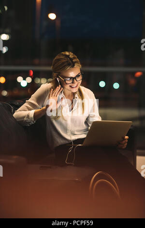 Businesswoman making a video call using a digital tablet in office lobby. Woman making gestures on a video call while working late in office. Stock Photo