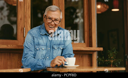 Portrait of happy retired man having coffee at coffeeshop. Smiling senior man relaxing at cafe. Stock Photo