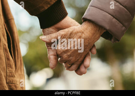 Close up of elderly couple holding hands and walking outdoors. Rear view of man and woman holding hands of each other while walking outdoors. Stock Photo