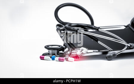 Green stethoscope with pile of antibiotic capsule pills on white table near drug tray. Antimicrobial drug resistance and overuse. Medical equipment fo Stock Photo