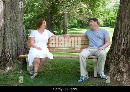 A happily married man and woman sit together on a park bench and look affectionately at one another Stock Photo