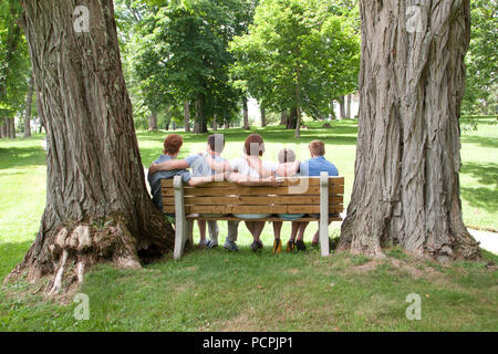 A lovely family of gingers sits together on a park bench viewed from the back Stock Photo