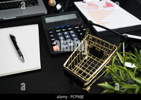 The concept of online shopping. Gold cart, cash and gadgets on a black table. Stock Photo