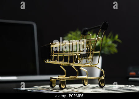 The concept of online shopping. Gold cart, cash and gadgets on a black table. Stock Photo