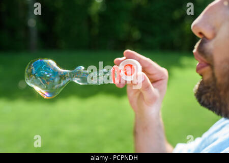 side view of bearded man blowing soap bubbles in park Stock Photo