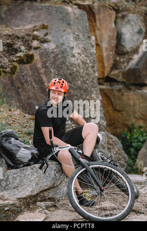 happy young trial biker relaxing on rocks with bicycle outdoors Stock Photo