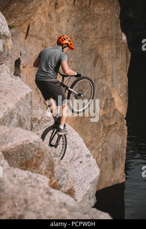 high angle view of trial biker balancing on back wheel on rocks outdoors
