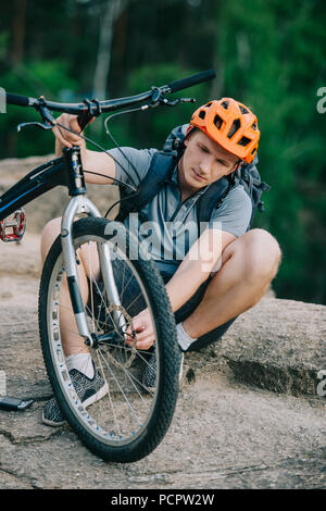 handsome young trial biker attaching wheel to bicycle outdoors Stock Photo