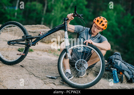 young trial biker attaching wheel to bicycle outdoors Stock Photo
