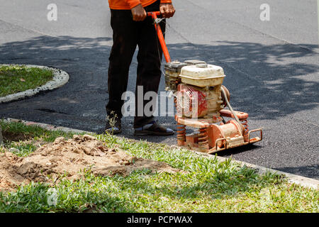 Worker uses vibratory plate compactor compacting asphalt at road repair Stock Photo