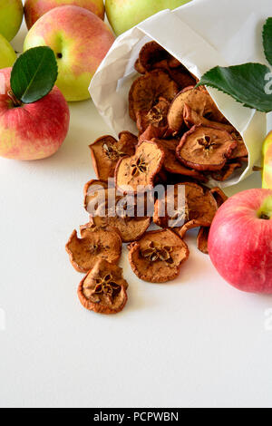 Tasty apple chips wrapped in paper on white wooden background Stock Photo