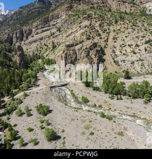 Small bridge crosses a river below massive mountains in the Rockies of Wyoming. Stock Photo