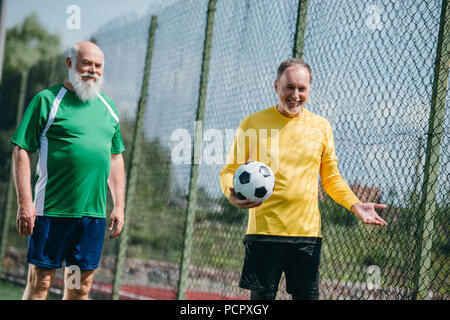 portrait of old smiling men in football uniform with football ball on field Stock Photo