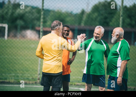 interracial elderly football players shaking hands after match on green field Stock Photo