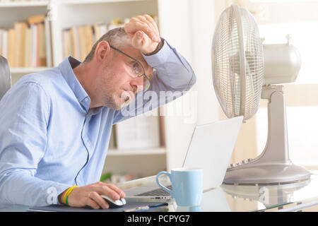 Man suffers from heat while working in the office and tries to cool off by the fan Stock Photo