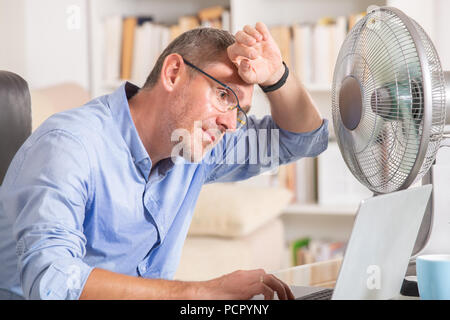 Man suffers from heat while working in the office and tries to cool off by the fan Stock Photo