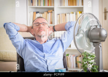 Man suffers from heat while working in the office and tries to cool off by the fan Stock Photo