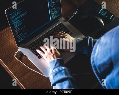 overhead hacker in the hood working with laptop and mobile phone typing text in dark room Stock Photo
