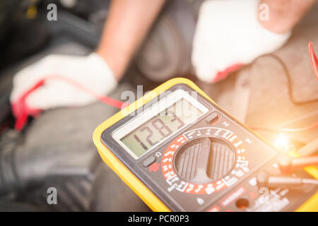 Car mechanic uses a multimeter to check car battery voltage Stock