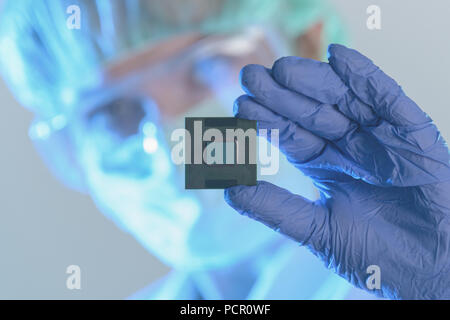 An engineer working in a laboratory wearing a special uniform and protective gloves holds new processor in hands and examines it Stock Photo
