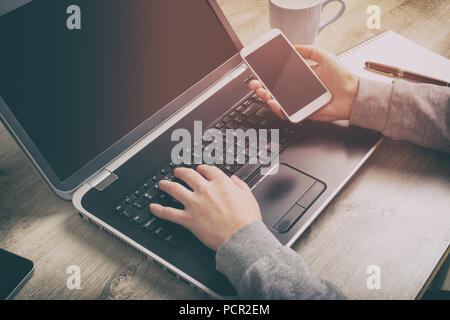 Concept of modern working style. Hand holding smartphone and other one on laptop keyboard Stock Photo