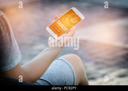 Smartphone with modern fortunetelling tarot application on screen. Woman is using this app outside. Stock Photo