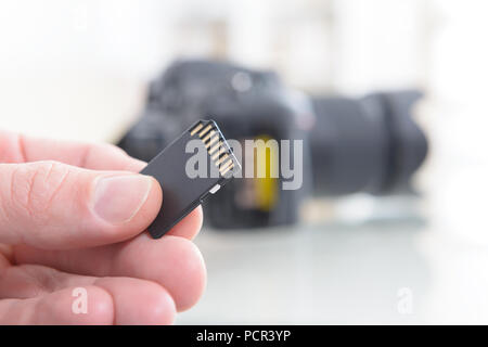 Hand holdnig sd memory card, DSLR in the background Stock Photo