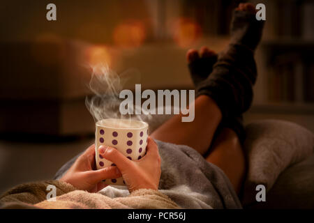 Woman with cup of hot drink  and feet lying on pilow in the cozy room