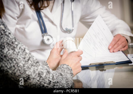 Patient holding a bottle of pills and doctor making notes in background Stock Photo