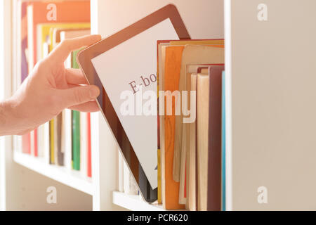 Man taking modern ebook reader from a bookshelf. Stock Photo