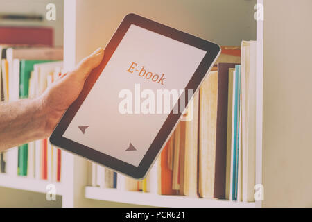 Man taking modern ebook reader from a bookshelf. Stock Photo