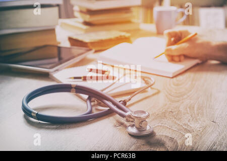 Young doctor is learning and preparing for the exam, he is using books and tablet to search for knowledge and making notes Stock Photo