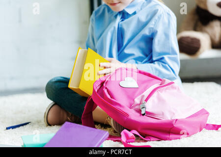 cropped shot of smiling child holding book while packing school bag Stock Photo
