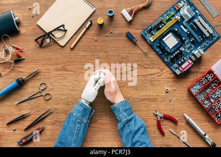 cropped image of electronic engineer with robotic hand sitting at table with instruments and motherboard Stock Photo