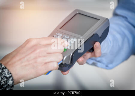 Entering PIN code on wireless payment terminal with inserted redit or debit card Stock Photo