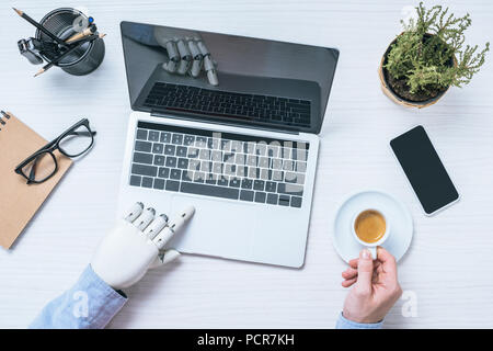 cropped image of businessman with prosthetic arm using laptop and holding coffee cup at table Stock Photo