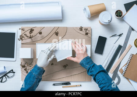partial view of male architect with prosthetic arm making model of house at table Stock Photo