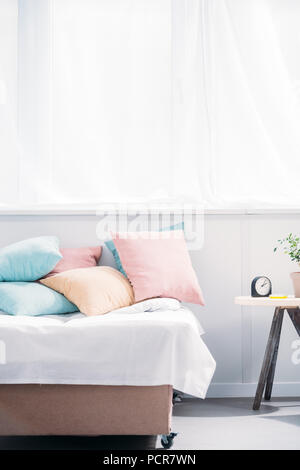 bed with lot of pillows in modern light room with alarm clock and plant of bedside table Stock Photo