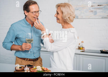 happy senior couple drinking wine and eating delicious snacks at home Stock Photo