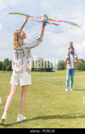 young woman holding colorful kite while father carrying little daughter on neck Stock Photo