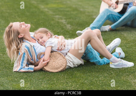 cropped shot of father playing guitar while mother and daughter hugging on grass