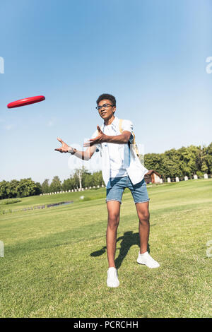 full length view of african american teenager with backpack playing with flying disc in park Stock Photo